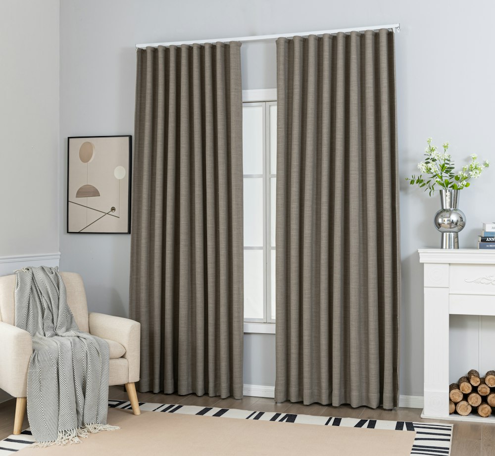 Referencia de una zona de descanso con cortinas beige y una butaca para el concepto Alba.